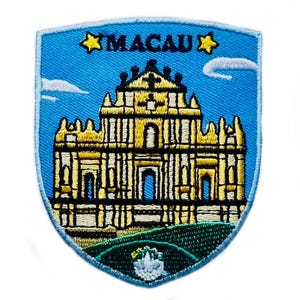 May include: Embroidered patch depicting a yellow building with blue doors and windows, set against a blue sky with white clouds. The patch is shield-shaped and features the word "MACAU" with star accents.
