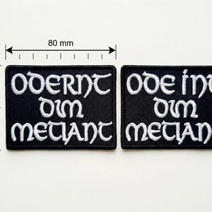 Könnte beinhalten: Zwei schwarze, gestickte Aufnäher, jeweils 80 mm breit und 50 mm hoch. Die Aufnäher zeigen weißen Text in einer stilisierten Schriftart. Der Text auf dem linken Aufnäher lautet "Oderint dum metuant", und der rechte Aufnäher lautet "Odeint dum metiant".