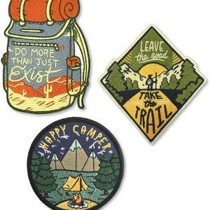 May include: Three embroidered iron-on patches with a camping theme. The first patch is a green, yellow, and orange backpack with the text "Do more than just exist". The second patch is a diamond shape with a green, yellow, and orange mountain scene and the text "Leave the road take the trail". The third patch is a round patch with a green, yellow, and orange scene of a campsite with the text "Happy Camper".