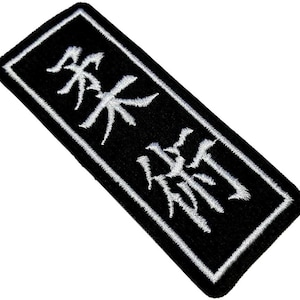 Könnte beinhalten: Schwarzer rechteckiger Aufnäher mit weißen, gestickten japanischen Schriftzeichen und weißem Rand. Der Aufnäher ist abgewinkelt und zeigt die detaillierten Stickereien. Der Text ist klar und lesbar.