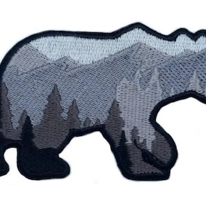 May include: Embroidered iron-on patch featuring a black bear silhouette with a mountain and forest scene inside. The bear is walking to the right. The mountains and trees are in shades of grey.
