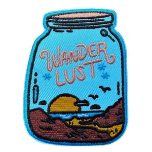 Op de afbeelding: Een blauwe geborduurde patch in de vorm van een pot met de woorden "Wanderlust" in roze letters. De pot bevat een zonsondergangsscene met een gele zon, blauw water en bruin zand.