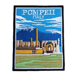Peut inclure: Un patch brodé avec un fond bleu et un texte blanc qui dit "POMPEII ITALIE". Le patch représente une image stylisée des ruines de Pompéi avec une montagne en arrière-plan.