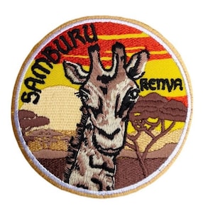 May include: A round embroidered patch with a yellow background and a sunset scene. The patch features a giraffe with a brown and black patterned coat, looking directly at the viewer. The text "SAMBURU" is written in black on the left side of the patch, and "REIMA" is written in black on the right side of the patch.