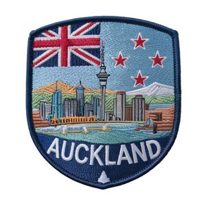 May include: Embroidered patch featuring the Auckland skyline, the New Zealand flag, and the text "AUCKLAND." The patch has a blue border and a light blue background with four red stars. The design includes a mountain range and a body of water.