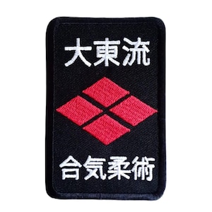 Op de afbeelding: Zwarte geborduurde patch met witte tekst die "大東流 合気柔術" luidt. De patch heeft een rode ruitvorm met vier kleinere ruiten erin.