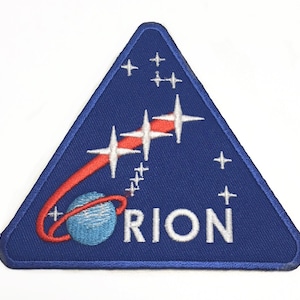 Könnte beinhalten: Ein blauer dreieckiger Patch mit einem roten und weißen Kometen, einem blauen Globus und dem Wort "ORION" in weißen Buchstaben.