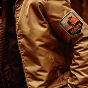 May include: A brown bomber jacket with a patch on the sleeve that says "MARS EXPLORER" with a graphic of a person standing on a red planet.