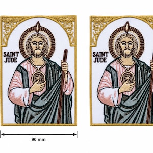 Könnte beinhalten: Zwei gestickte Aufnäher mit dem heiligen Judas. Jeder Aufnäher ist 12,5 cm hoch und 9 cm breit. Das Bild zeigt den heiligen Judas mit Heiligenschein und Stab, mit dem Text "SAINT JUDE". Die Aufnäher haben goldene und weiße Ränder. Religiöses Thema.