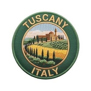 Könnte beinhalten: Gestickter Aufnäher mit einer Landschaft der Toskana, Italien. Der Aufnäher hat einen grünen Rand mit den Wörtern "TUSCANY" und "ITALY" in Gold. Das zentrale Bild zeigt ein Gebäude, Bäume und Felder in Gelb-, Grün- und Brauntönen.
