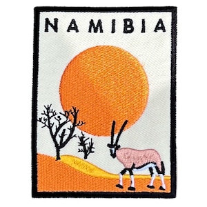 May include: An embroidered patch with a black outline, featuring a stylized orange sunset over a desert landscape with a black silhouette of a tree and an oryx. The text "NAMIBIA" is at the top of the patch.