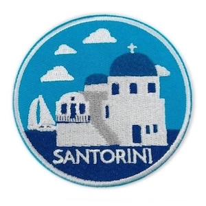 May include: A blue and white embroidered patch with a white building with a blue dome and a white sailboat in front of it. The text "SANTORINI" is below the building.
