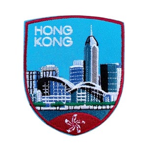 Op de afbeelding: Een geborduurde patch met een blauwe achtergrond met een skyline van Hongkong met de tekst "HONG KONG" in wit. De patch heeft een rode rand en een rood-witte vlag van Hongkong in het midden onderaan.