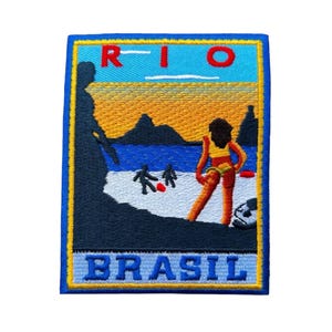 May include: Embroidered patch depicting a beach scene with the text "RIO BRASIL". The design includes a woman in a yellow bikini, a beach, ocean, and mountains under a sunset sky. The patch has a blue border with yellow accents.