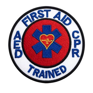 May include: Embroidered patch with the words "FIRST AID CPR TRAINED AED" in blue and white. The center features a red circle with a blue star of life and a yellow heart.