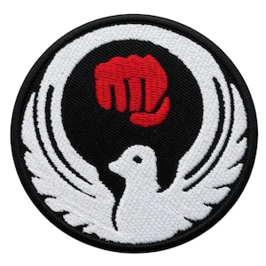 May include: Round embroidered patch with a black background. It features a white dove with outstretched wings and a red fist inside a white circle. The patch has a black border.