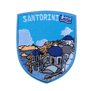 May include: Embroidered patch featuring a blue and white Greek flag, the word "SANTORINI" in white text, and an embroidered image of white buildings with blue domes on a cliff overlooking the ocean.