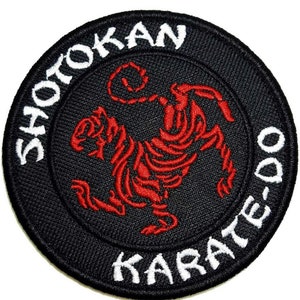 Op de afbeelding: Een geborduurde patch in zwart en wit met een rode tijger in een vechtpose. De woorden "Shotokan Karate-Do" staan in een cirkel rond de tijger.