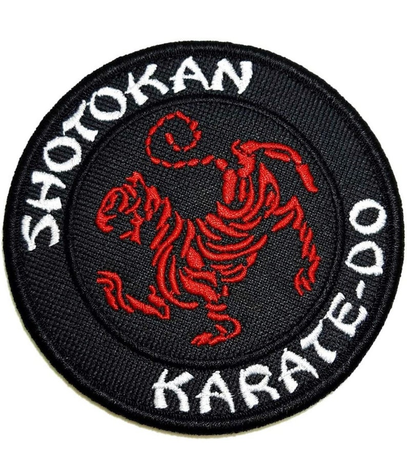 Op de afbeelding: Een geborduurde patch in zwart en wit met een rode tijger in een vechtpose. De woorden "Shotokan Karate-Do" staan in een cirkel rond de tijger.