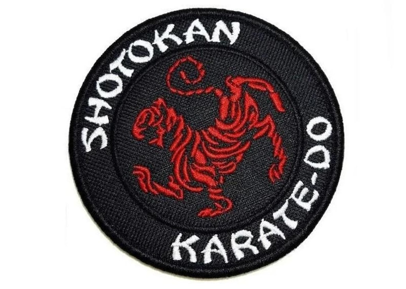 Op de afbeelding: Een geborduurde zwarte en witte patch met een rode tijger in het midden. De patch heeft de tekst "Shotokan Karate-Do" in witte letters.