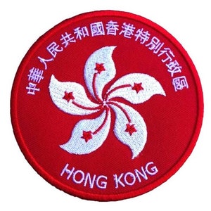 May include: A red embroidered patch featuring the Hong Kong flag, a white bauhinia flower with five petals and five stars, and the text "HONG KONG" in white. The text surrounding the flag reads "中華人民共和國香港特別行政區".