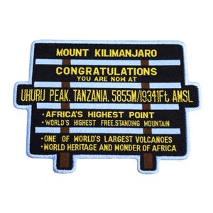 Peut inclure: Un écusson rectangulaire noir avec du texte blanc et jaune. L'écusson indique "MOUNT KILIMANJARO" et "CONGRATULATIONS YOU ARE NOW AT UHURU PEAK, TANZANIA. 5855m/19341ft AMSL". Il indique également "AFRICA'S HIGHEST POINT".