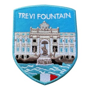 Pode incluir: Patch bordado com a Fontana di Trevi em Roma. O patch tem a forma de um escudo azul claro com as palavras "TREVI FOUNTAIN" no topo. A fonte é retratada em detalhes, com uma base de água azul e a bandeira italiana na parte inferior.