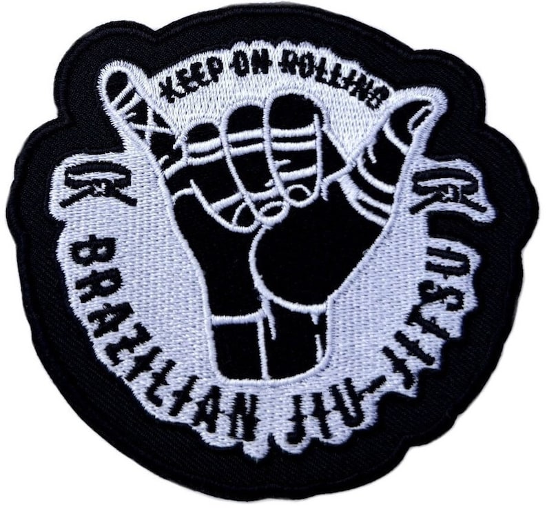 May include: Black and white embroidered patch with a hand making the shaka sign. The text around the hand reads "Keep on Rolling Brazilian Jiu-Jitsu".