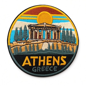 Op de afbeelding: Een ronde geborduurde patch met een afbeelding van het Parthenon in Athene, Griekenland. Het ontwerp bevat een gele zon, een blauwe lucht, groene cipressen en beige stenen structuren. De tekst ATHENS GREECE is geborduurd in geel en grijs.