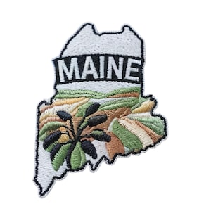 May include: Embroidered patch in the shape of the state of Maine, with the word "MAINE" in white block letters. The patch features a landscape design with green, brown, and tan colours, and a black and green plant.