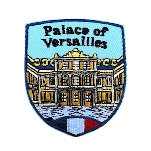 Könnte beinhalten: Gestickter Aufnäher mit dem Schloss Versailles. Der Aufnäher hat einen hellblauen Hintergrund mit den Worten "Palace of Versailles" in Schwarz. Das Schloss ist in Gold, Braun und Weiß dargestellt, mit einer französischen Flagge unten.