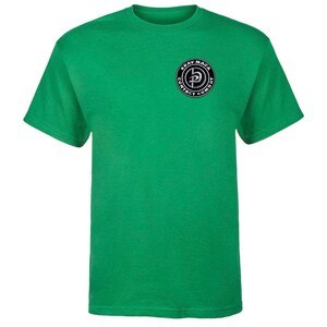 K&ouml;nnte beinhalten: Ein gr&uuml;nes T-Shirt mit kurzen &Auml;rmeln und einem schwarz-wei&szlig;en Krav Maga Contact Combat Logo auf der linken Brust.