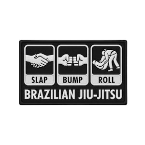 May include: Black rectangular patch with white graphics and text. The patch features three panels with illustrations of a handshake, fist bump, and a person grappling. The text reads "SLAP", "BUMP", "ROLL", and "BRAZILIAN JIU-JITSU".