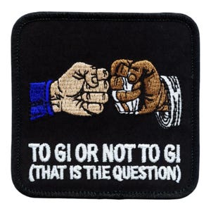 Pode incluir: Patch quadrado preto com design bordado. Dois punhos batendo, um com manga azul, o outro com manga listrada. O texto diz "TO GI OR NOT TO GI (THAT IS THE QUESTION)" em branco.