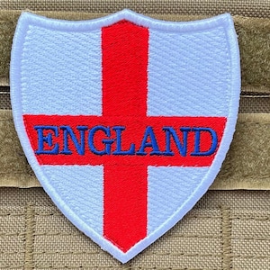 May include: White embroidered patch with a red cross and the word "ENGLAND" in blue lettering. The patch is shaped like a shield.