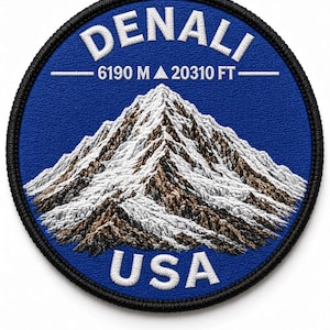 May include: A circular embroidered patch featuring a blue background with a white mountain peak illustration. The text reads DENALI at the top, 6190 M 20310 FT in the center, and USA at the bottom. The patch has a thick black stitched border.