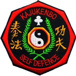 May include: A black and red octagonal patch with the words "Kajukenbo Self Defence" in white lettering. The patch features a yin yang symbol with a green wreath and a white clover.