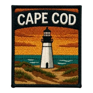 May include: A rectangular embroidered patch featuring a white lighthouse standing on sandy dunes with green grass. The background shows a teal ocean and an orange sunset sky. The text CAPE COD is stitched in white letters at the top on a black border.
