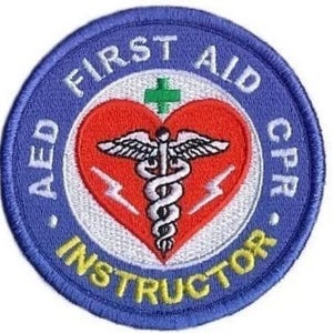 May include: Blue and yellow embroidered patch with a white circle containing a red heart with a medical symbol and the words "First Aid CPR AED Instructor".