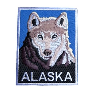 May include: Embroidered patch featuring a white wolf with a blue background. The text "ALASKA" is embroidered in white on a black background.