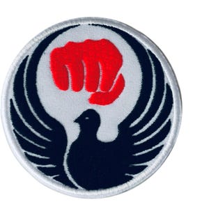 May include: Circular patch with a white background, a red fist, a black bird, and black wings. The patch has a white border and is likely an emblem or logo.