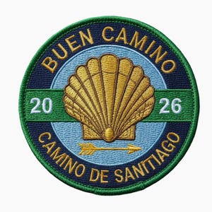 Peut inclure: Écusson brodé circulaire avec une coquille Saint-Jacques dorée. Le texte "BUEN CAMINO" et "CAMINO DE SANTIAGO" est présent, ainsi que les chiffres "20" et "26". Le patch est bleu, vert et or.