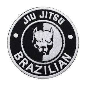 Può includere: Toppa ricamata in bianco e nero con la scritta "Jiu Jitsu Brazilian" in un design circolare. La toppa presenta una testa di cane stilizzata al centro, con uno sfondo diviso. Due punti bianchi sul bordo esterno.