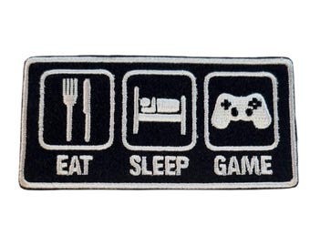 May include: Black rectangular patch with white embroidered icons and text. The patch features a fork and knife, a bed, and a game controller, with the words "EAT", "SLEEP", and "GAME" below each icon, respectively.