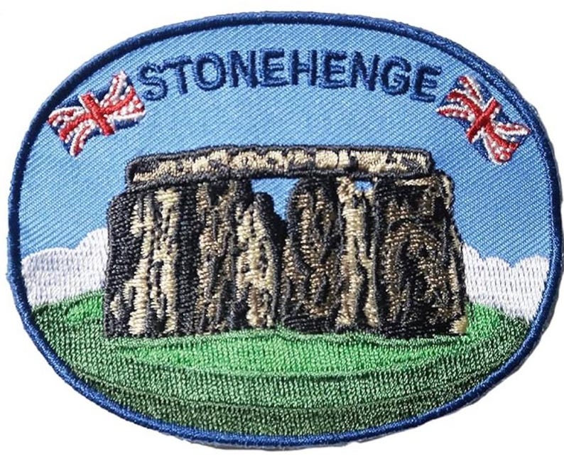 K&ouml;nnte beinhalten: Ovaler, gestickter Aufn&auml;her mit Stonehenge und dem Text "STONEHENGE" in Blau. Der Aufn&auml;her hat einen blauen Hintergrund, zwei Union Jack-Flaggen und eine gr&uuml;ne Wiese am unteren Rand.