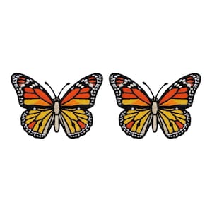 Op de afbeelding: Twee geborduurde vlinderpatches. Elke vlinder heeft oranje, gele en zwarte vleugels met witte accenten. De vlinderlichamen zijn beige en de patches hebben een zwarte rand. Op een witte achtergrond.