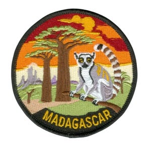 Könnte beinhalten: Runder, gestickter Aufnäher mit einem Lemuren auf einem Ast, vor einer Sonnenuntergangskulisse mit Baobab-Bäumen. Das Wort "MADAGASCAR" ist am unteren Rand gebogen. Der Aufnäher hat einen schwarzen Rand.