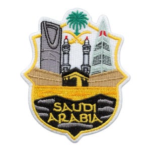 May include: Embroidered patch featuring landmarks of Saudi Arabia. The design includes a building, minarets, a palm tree, and the text "SAUDI ARABIA" in gold lettering. The patch has a shield shape with a yellow border.