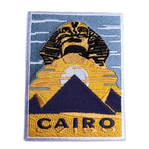 Könnte beinhalten: Gestickter Aufnäher mit blauem Hintergrund, der eine gelbe Silhouette der Großen Sphinx von Gizeh und der Pyramiden von Gizeh zeigt. Der Text "CAIRO" ist unten auf dem Aufnäher in Gelb gestickt.