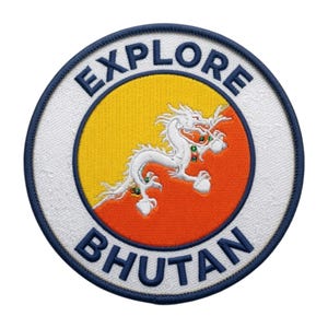 Peut inclure: Un écusson brodé circulaire représentant un dragon blanc sur un fond jaune et orange. Le texte EXPLORE est inscrit en arc de cercle en haut et BHUTAN en bas en lettres bleu foncé. L'écusson possède une bordure bleu foncé.